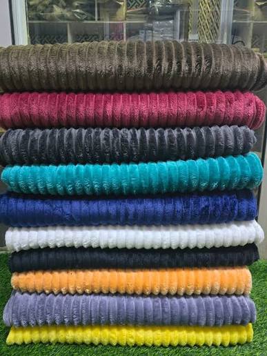 Assorted wholesale blanket fabrics – fleece (soft), cotton (breathable), and acrylic (durable) stacked for bulk order inspection in Kampala.